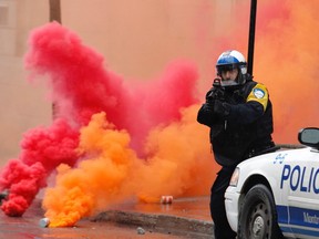 A police officer stands guard after firing tear gas on anti-capitalist demonstrators who had thrown coloured smoke bombs as they marched through the streets of  Montreal on Sunday, May 1, 2016.