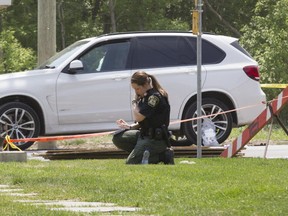 A Laval police officer takes notes at the scene of a fatal shooting on Boulevard St-Elzéar West, Laval, north of Montreal, Friday May 27, 2016, in which Rocco Sollecito, 67, long affiliated with the Mafia, was killed. Police believe the suspect waited in the bus shed for Sollecito, driving the white BMW SUV, to arrive.