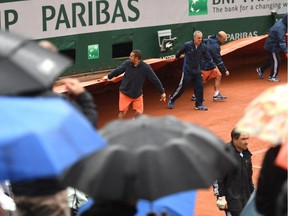 Ground staff pull on the covers as rain causes play to be abandoned for the day on day one of the 2016 French Open at Roland Garros on May 22, 2016, in Paris.