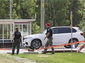A pair of Laval police officers survey the scene of a fatal shooting on Boulevard Saint Elzéar West, in Laval, north of Montreal, Friday May 27, 2016, in which Rocco Sollecito, 67, long affiliated with the Rizzutos, was killed.  Police believe the suspect waited in the bus shed for Sollecito, driving the white BMW SUV, to arrive.