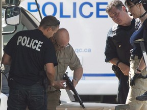 Montreal police officers look at a weapon seized from a house in Montreal, Wednesday, July 31, 2013, following a standoff with an armed man. Twenty-one years after the introduction of the federal long-gun registry -- since abolished by the Conservatives -- Quebec is making progress on creating its own database of non-restricted firearms.