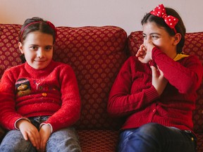 Six year-old Ilaf Al Jayoush, left, and her sister Alyaa Al Jayoush, 10, smile as they sit on the couch at their aunt's home in Montreal.