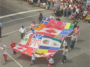 A large Canadian flag surrounded by provincial and territorial flags turns the corner from Ste-Catherine St. to Peel St. during the Canada Day parade in Montreal in 2004.