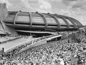 Crowds sit on hillside on north side of Olympic stadium July 17, 1976 in Montreal as they await the arrival of Olympic teams along roadway to left.