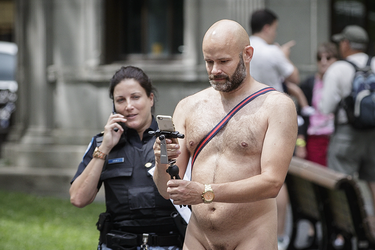 A police officer glances at a man as he takes part in the World Naked Bike Ride at Dorchester Square in Montreal on Saturday, July 16, 2016. The World Naked Bike Ride event aims to encourage cycling, promote environmentalism, and address body image issues.