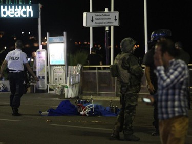 A police officer stands next to a dead body covered with a blue sheet on the Promenade des Anglais seafront in the French Riviera town of Nice on July 15, 2016, after a van drove into a crowd watching a fireworks display. At least 75 people were killed when a truck drove into a crowd watching a fireworks display in the French resort of Nice, a lawmaker said on July 15.
