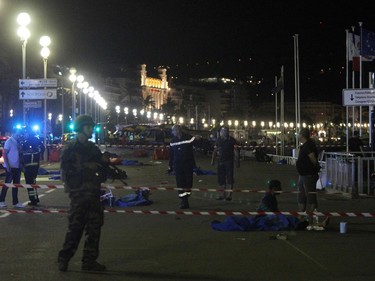 Soldiers, police officers and firefighters walk near dead bodies covered with a blue sheets on the Promenade des Anglais seafront in the French Riviera town of Nice on July 15, 2016, after a van drove into a crowd watching a fireworks display. At least 75 people were killed when a truck drove into a crowd watching a fireworks display in the French resort of Nice, a lawmaker said on July 15.