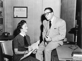 George Reeves, as Clark Kent, sits on desk beside Noel Neill, as Lois Lane, in a still from the television series Adventures of Superman, c. 1955.