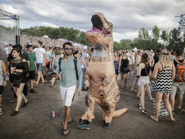 A man wearing a dinosaur costume walks through the festival grounds during Day One of the Osheaga Music and Arts Festival at Parc Jean-Drapeau in Montreal on Friday, July 29, 2016.