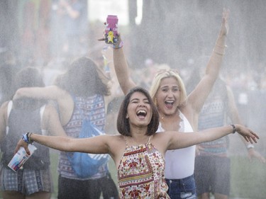 Toronto visitors Ruda, left, and Justine, right, dance under water mist during Day One of the Osheaga Music and Arts Festival at Parc Jean-Drapeau in Montreal on Friday, July 29, 2016.