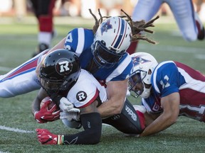 Ottawa Redblacks running-back Travon Van is tackled by Montreal Alouettes linebacker Bear Woods, top, and linebacker Chip Cox during first quarter CFL football action, in Montreal on Thursday, June 30, 2016.