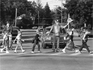 1985: a crossing guard keeps things moving safely, at a time when backpacks were not worn by all, nor were they the equivalent to a ball and chain.