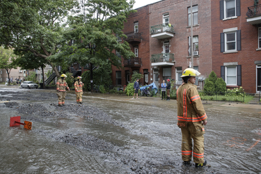 Firefighters walk through a flooded Brewster avenue near the corner of St-Antoine street at the scene where a water main break caused flooding in the borough of St-Henri in Montreal on Saturday, August 13, 2016.