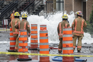 Firefighters look at a geyser of water caused by a water main break on the corner of St-Antoine street and Brewster avenue in the borough of St-Henri in Montreal on Saturday, August 13, 2016.