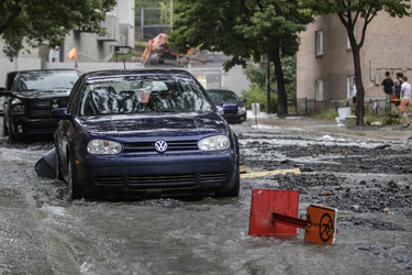 A vehicle is surrounded by water on Brewster avenue near the corner of St-Antoine street at the scene where a water main break caused flooding in the borough of St-Henri in Montreal on Saturday, August 13, 2016.