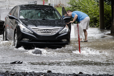 A man checks his vehicle for flooding on Brewster avenue near the corner of St-Antoine street at the scene where a water main break caused flooding in the borough of St-Henri in Montreal on Saturday, August 13, 2016.