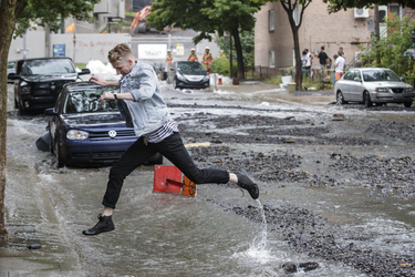 A man jumps the over water on Brewster avenue near the corner of St-Antoine street at the scene where a water main break caused flooding in the borough of St-Henri in Montreal on Saturday, August 13, 2016.
