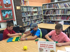 Eleven-year-old Healey twins Thomas (in red shirt) and Liam (in pink shirt) brought baseball buddy Daniel Sylvestre, 11, to his first yarn-bombing session at the Beaconsfield Public Library, Aug. 3, 2016. Photo credit: Montreal Gazette