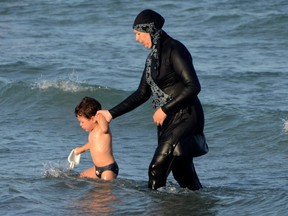 A Tunisian woman wearing a "burkini", a full-body swimsuit designed for Muslim women, walks in the water with a child on August 16, 2016 at Ghar El Melh beach near Bizerte, north-east of the capital Tunis.