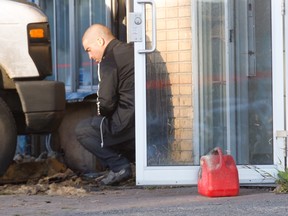 A Montreal police investigator squats beside a fuel jug as he examines damage at a food distribution warehouse in St-Léonard, Montreal, Friday September 16, 2016.  Police say an accelerant was used. It's the second arson in as many days.