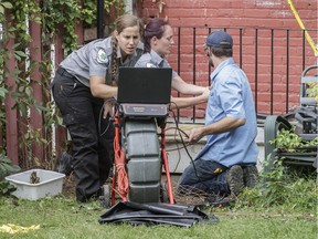 Animex animal technicians Eve Surprenant Desjardins, left, and Ariane Duplessis, centre, look at a screen with a video feed from a fiberoptic camera at the location where they thought an escaped python was hiding under a home located on Willibrord street in Verdun in Montreal on Wednesday, August 31, 2016.