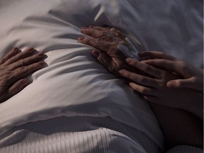Daughter touching hands of her mother lying in a hospital bed.