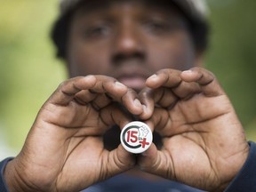 Montreal Old Port worker Konrad Lamour holds up a badge illustrating a demand for a minimum hourly wage of $15 in Montreal on Friday, Oct. 14, 2016.