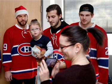 Montreal Canadiens left wing Phillip Danault, centre, holds Laurie Ann Michaud as her mother, Chantal Archambault, tries to take a picture during the Montreal Canadiens annual visit to the Montreal Children's Hospital in Montreal on Wednesday Dec. 14, 2016. Montreal Canadiens defenceman Andrei Markov, left, and centre Alex Galchenyuk are also seen.