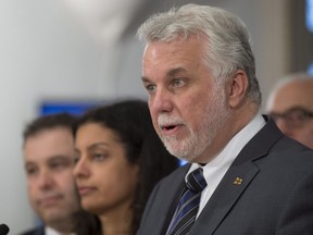 Quebec Premier Philippe Couillard speaks at a news conference marking the end of the fall session at the National Assembly, in Quebec City on Friday, December 9, 2016. Quebec Education and Family Minister Sebastien Proulx, left, and Quebec Economy, Science and Innovation Minister Dominique Anglade, centre, look on.