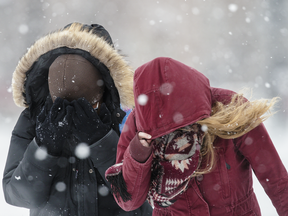 Cegep Maisonneuve students Sokito Som, left, and Frederique Emond, right, shield themselves from the blowing snow as they walk on Pierre-de-Coubertin ave in Montreal on Tuesday, Jan. 24, 2017.