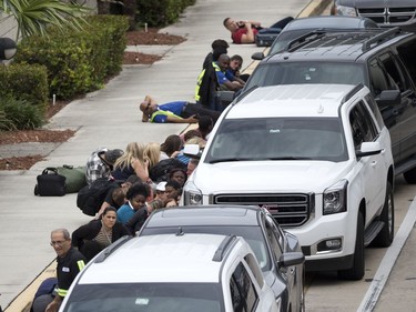 People take cover outside Fort Lauderdale–Hollywood International Airport, Friday, Jan. 6, 2017, in Fort Lauderdale, Fla., after a shooter opened fire inside a terminal of the airport, killing several people and wounding others before being taken into custody.