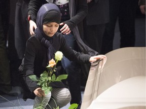 A young girl places a flower next to one of the caskets during a ceremony for three of the six victims of the Quebec City mosque shooting Friday, February 3, 2017 in Quebec City.