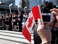 A woman takes a photograph while holding a Canadian flag during a citizenship ceremony.