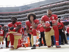 San Francisco 49ers quarterback Colin Kaepernick is flanked by outside linebacker Eli Harold, left, and safety Eric Reid during the national anthem before an NFL football game in 2016. The trio were kneeling to protest oppression against African Americans.