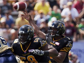 Hamilton Tiger-Cats quarterback Henry Burris, right, gets some protection from teammate Brian Simmons, left, as he makes a pass during first quarter CFL action as the Tiger-Cats take on the Winnipeg Blue Bombers in Guelph, Ont., Saturday, August 24, 2013.