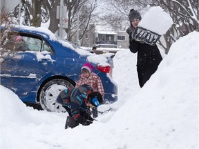 Sophie Fanna, right, cleans her driveway on Matis St. in Ville-St-Laurent Feb. 13, 2017, as children, Noemie Busque, 6, left, Marina Busque, 2 and Antoine Busque, 5, foreground, play, following a snowstorm that dumped up to 23cm of snow in some places.