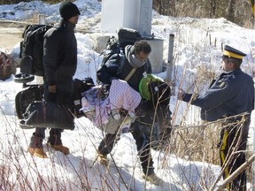 RCMP officers help a group of asylum seekers cross a ditch as they crossed from the U.S. into Canada illegally at Roxham Rd., near Hemmingford, Que., on Monday, Feb. 20, 2017.  There has been a spike in the number of asylum seekers entering Canada in recent weeks, with most crossing into Quebec, primarily at this location.