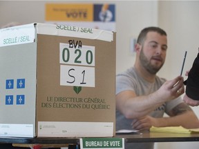 An Elections Quebec official hands a pen to a woman as she prepares to cast her ballot at an advance polling station.