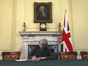 Britain's Prime Minister Theresa May, sitting below a painting of Britain's first Prime Minister Robert Walpole, signs the official letter to European Council President Donald Tusk, in 10 Downing Street, London, Tuesday March 28, 2017, invoking Article 50 of the bloc's key treaty, the formal start of exit negotiations. Britons voted in June to leave the bloc after four decades of membership. (Christopher Furlong/Pool Photo via AP) ORG XMIT: LON122
