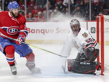 Chicago Blackhawks Corey Crawford winces as Montreal Canadiens Dwight King kicks up ice spray while crashing the net during first period of National Hockey League game in Montreal Tuesday March 14, 2017.