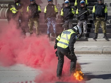 A police officer extinguishes a smoke canister thrown by an anti-racist protester in front of Montreal city hall Saturday, March 4, 2017.