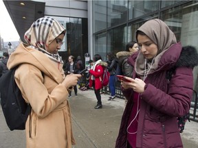 Concordia University students Sarah Ab, left, and Yasmina Elzagheid browse their cellphones outside the university in Montreal, Wednesday, March 1, 2017, following a bomb threat against Muslim students.