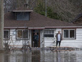 A couple watch the river water flow past their home on Île-Mercier in Ile-Bizard on Thursday, April 20.