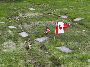 Shirley Elgar-Murdock places a Canadian flag and and American flag on the gravestone of her parents; her mother, Anna Aitken, was born in the U.S.