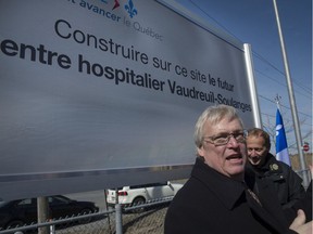 Quebec Health Minister Gaetan Barrette stands in front of the sign announcing a planned new hospital to serve the Vaudreuil-Soulanges region on April 4, 2016.