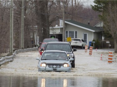 Cars move along a street in the town of Rigaud, Que., west of Montreal, Thursday, April 20, 2017, following flooding in the area. A state of emergency has been issued for the town.