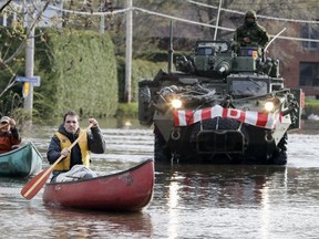 Alain Leroux, right, and Bernard Bégin paddle their canoes to pick up supplies on Blvd. du Lac in Deux Montagnes, northwest of Montreal as Canadian army personnel deliver sandbags Monday, May 8, 2017.