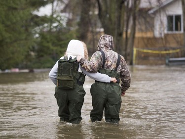 A couple walks through the flooded streets in the Île-Mercier district of Île-Bizard, Que. Friday, May 5,2017. Forecasts are calling for several more days of rain. THE CANADIAN PRESS/Ryan Remiorz