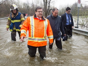 Montreal Mayor Denis Coderre walks through the flooded streets of the Ile-Mercier district of Ile-Bizard, Que., on Friday, May 5, 2017. Forecasts are calling for several more days of rain.