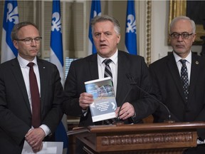 Quebec Transport Minister Laurent Lessard, centre, flanked by Quebec Public Security Minister and Municipal Affairs Minister Martin Coiteux, left and Quebec Finance Minister Carlos Leitão holds a copy of the government's plan at a news conference on Montreal's metropolitan electrified train project, Thursday, May 11, 2017 at the legislature in Quebec City.